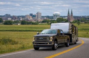 Heavy-duty pickup truck towing a fifth wheel RV through a scenic mountain valley.
