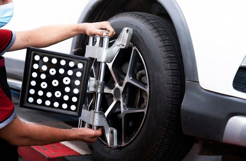 Technician performing wheel alignment on a car using an alignment machine attached to the front tire in an auto repair shop.